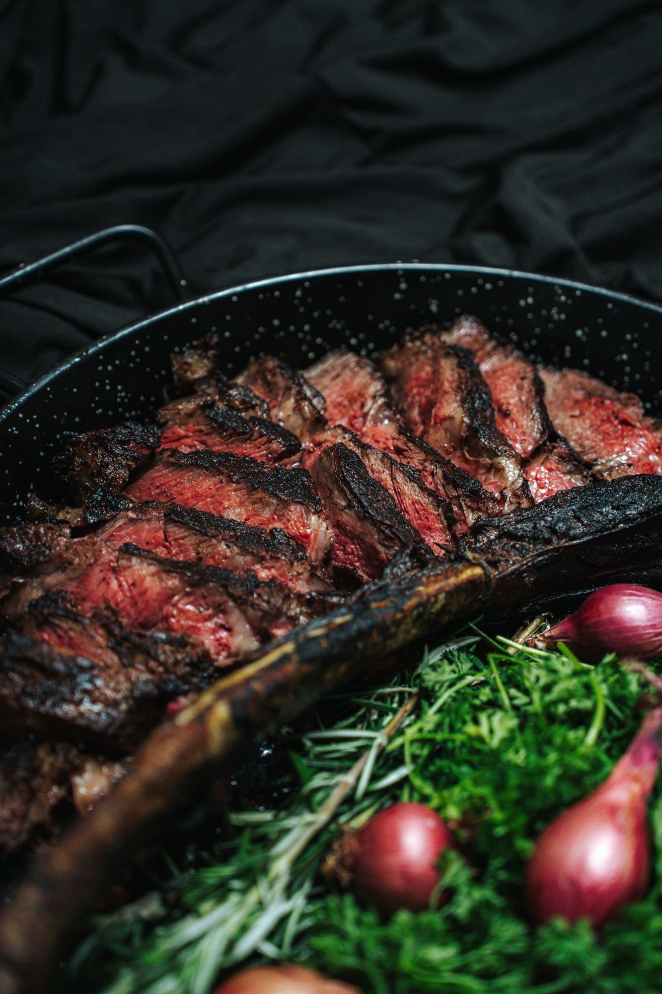 Sliced tomahawk ribeye resting in a cast-iron pan with herbs